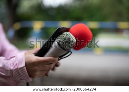 Professional woman journalist at event, holding microphones and recording notes on smartphone dictaphone