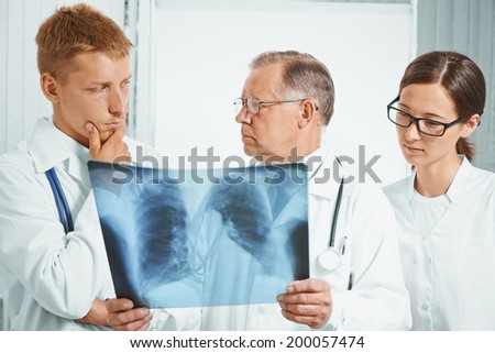 Professor older man doctor and young doctors examine x-ray image of lungs in a hospital