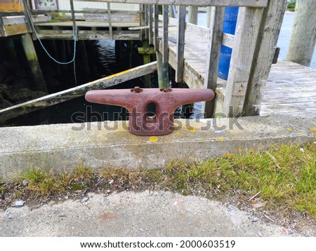 A boat docking station, or a cleat, that is used to tie up boats to keep them attached to the pier. Its metal, red, and in the shape of a letter T. The wharf is wooden and zig zags.