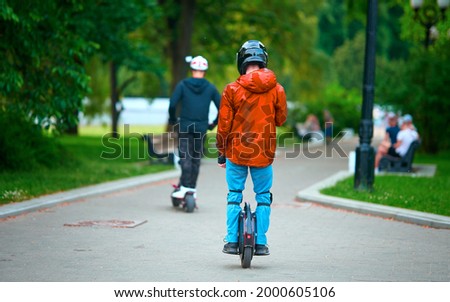 Man riding on unicycle in protective gear through public park. Young man with helmet and protective equipment rides on electric mono wheel in park on summer day. Urban individual transport Royalty-Free Stock Photo #2000605106