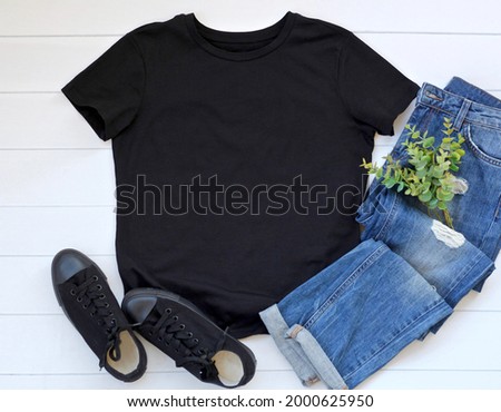 Black t shirt mock up flat lay on white wooden background. Top front view t shirt and copy space. Mockup t shirt with denim, eucalyptus and black shoes