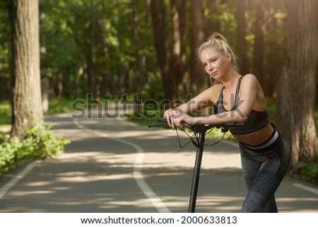Portrait of a girl with an electric scooter in sportswear in the park. An electric scooter is the most environmentally friendly means of transportation on the street. New types of transport in cities