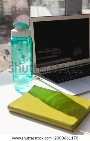 A bottle of water, a green diary on the background of a laptop workspace in a bright office