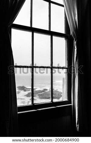 Old rustic light house window interior looking outside to the ocean. Lonely isolated feeling and dramatic lighting monochrome Royalty-Free Stock Photo #2000684900