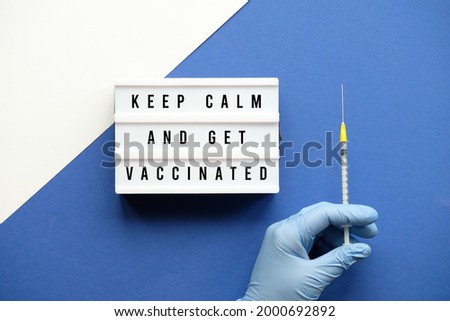 Vaccination motivator concept. Lightbox with text Keep Kalm and Get Vaccinated. Medic hand in glove with COVID 19, measles vaccine syringe. Creative monochrome flat lay on layered blue and white paper