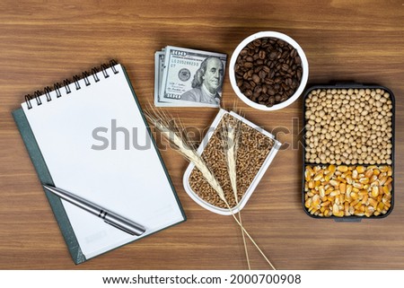 Top view mockup of open blank notebook on spiral, automatic pen. 100 dollar banknotes and samples of soybean, corn, wheat and coffee seeds, conceptualizing agricultural commodities. on a wooden table