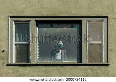 Woman covering her mouth with a bandana staring out the window during the coronavirus lockdown.