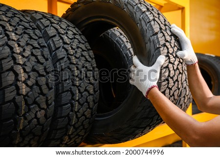 Asian male tire changer Checking the condition of off-road tires in stock so that they can be replaced at a workshop or auto repair shop. Tire warehouse for the car industry Royalty-Free Stock Photo #2000744996