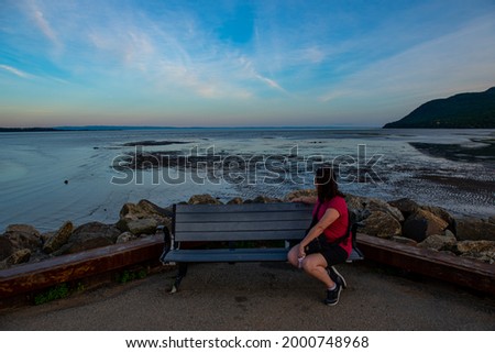 Woman on an outdoor bench looking back at the calm river with sunset in the background