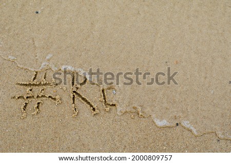 Concept of the End of Vacation.  Wave washes away the hashtag and the word REST on the yellow sand. Handwritten word on the wet sandy beach. Capital letters. View from above.