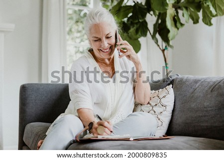 Cheerful elderly woman talking on a phone on a couch Royalty-Free Stock Photo #2000809835
