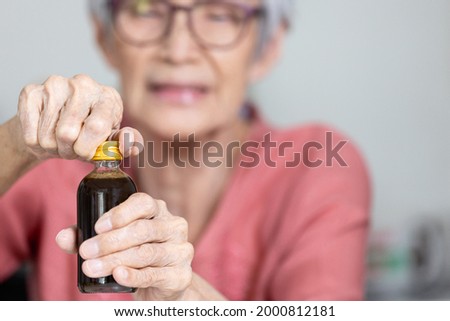 Asian senior woman trying hard to remove the screw cap,turn the bottle cap to open,trouble opening the lid of the bottle in the elderly aged or female people,difficulty in drinking,life problems