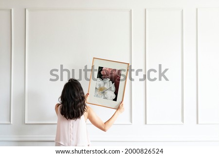 Curator hanging floral art frame on the wall Royalty-Free Stock Photo #2000826524