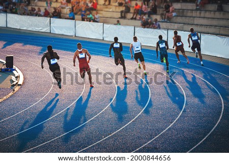 Sprinters running on the athletics Track in sunset light. Shadows on the track, Sprint, Track and Field photo, original wallpaper for games in Japan, Tokyo. Athletics meeting on blue track Royalty-Free Stock Photo #2000844656