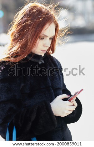 A beautiful unusual girl with red hair uses a mobile phone on the street,. High quality photo