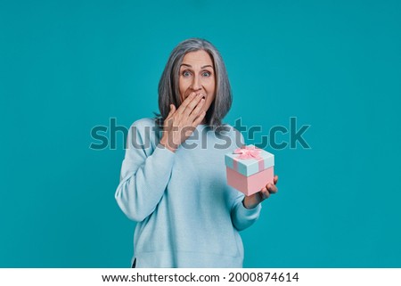 Mature beautiful woman holding gift box and covering mouth with hand
