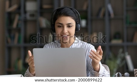 Confident millennial indian female coach tutor in modern headphone set explain academic program to remote students online. Young woman teacher speak give virtual lesson lecture before laptop webcam Royalty-Free Stock Photo #2000899622
