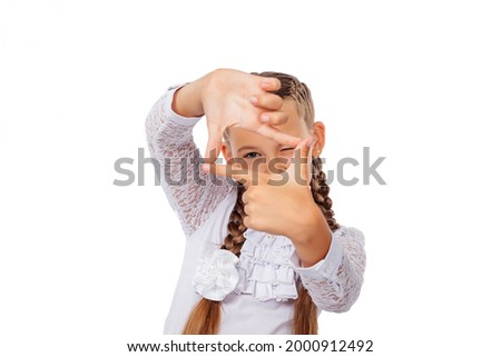 The schoolgirl looks through the frame from her fingers. A girl in a school uniform. Studio photo, isolated on a white background.