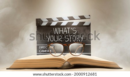 what's your story, text title on the film slate, and eyeglasses on top of the old book Royalty-Free Stock Photo #2000912681