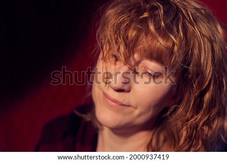 Portrait of smiling tousled disheveled middle-aged woman on red background. Unprofessional female model wiht smile posing in the Studio
