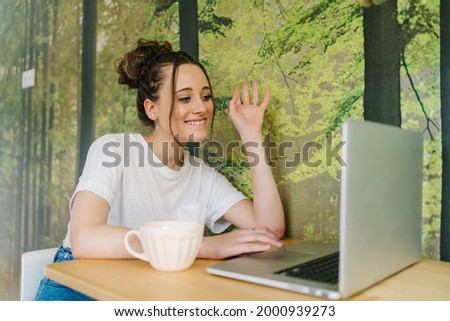 smiling young female creating content in living room with laptop and camera on tripod