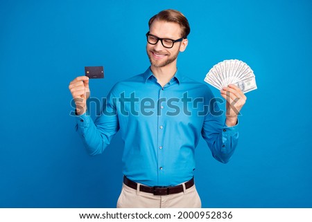 Photo of young business man happy positive smile hold bank card income money cash isolated over blue color background