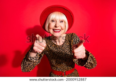 Photo of happy nice pretty old woman wear hat point fingers you mocking smile isolated on red color background