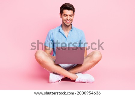 Photo of positive programmer guy sit floor work laptop wear blue shirt isolated on pink color background