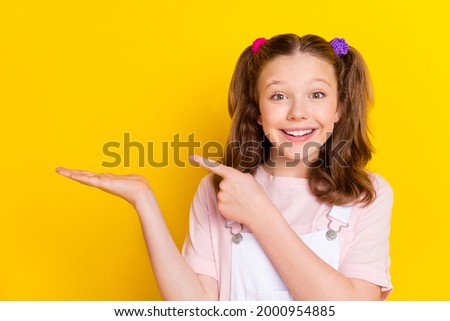 Photo portrait schoolgirl with tails showing empty space on palm isolated bright yellow color background