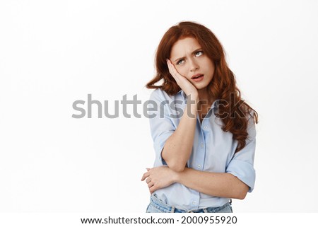 Bored and annoyed reluctant redhead student roll eyes, lean on hand and standing indifferent, attend boring meeting, standing bothered against white background