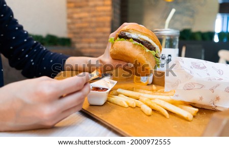 Hands holding fresh delicious burgers with french fries, sauce and beverage on the wooden table.Tasty grilled beef burger with lettuce and souse.