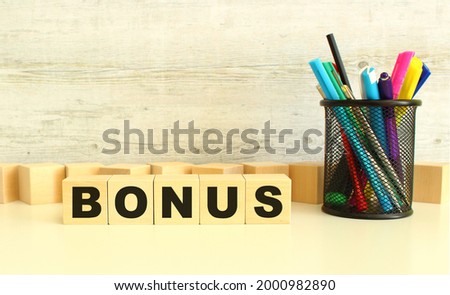 Five stacked wooden cubes with letters BONUS on a white desktop on a gray background.