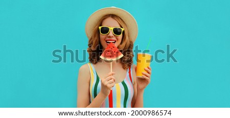 Summer portrait of happy smiling young woman with lollipop or ice cream shaped slice of watermelon and cup of juice wearing straw hat on blue background