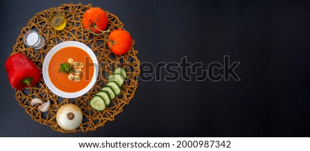Refreshing gazpacho surrounded by its ingredients on dark wooden table Royalty-Free Stock Photo #2000987342