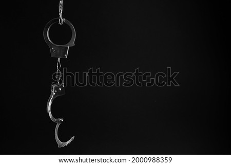 Classic chain handcuffs hanging on black background, space for text Royalty-Free Stock Photo #2000988359
