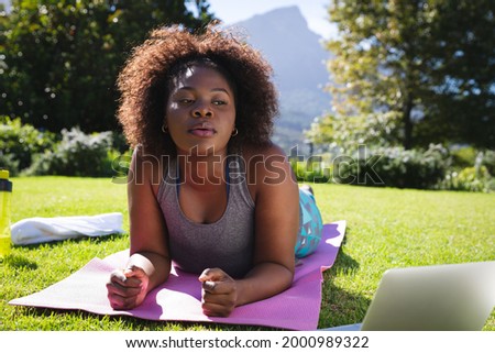 African american woman exercising doing lying on yoga mat in sunny garden. active lifestyle, outdoor fitness and leisure time.