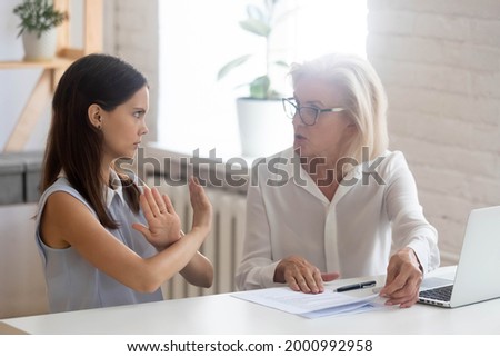 Diverse female colleagues work together with paperwork have misunderstanding at meeting. Young Caucasian woman worker refuse cooperate with middle-aged coworker. Teamwork problem concept. Royalty-Free Stock Photo #2000992958