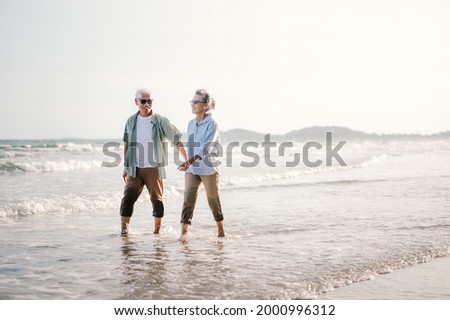Elderly Asian couple walking on the beach at sunset