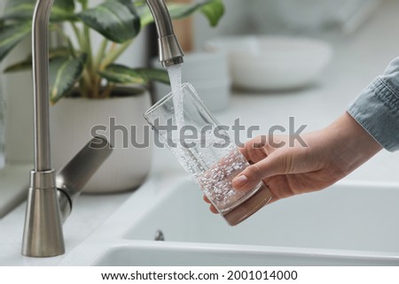 Woman filling glass with water from tap in kitchen, closeup Royalty-Free Stock Photo #2001014000