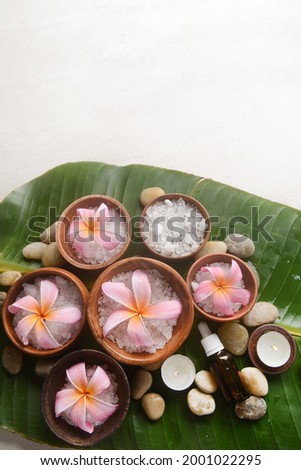 frangipani in bowl with white salt in wooden bowl ,oil bottle, candle stones with big leaves with wet drop background.
