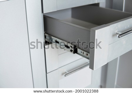 Stainless telescopic bayonet drawer slide guides, installed on a kitchen cabinet from gray chipboard. Accessories for carpentry used in the construction of furniture. Custom kitchen installation. Royalty-Free Stock Photo #2001022388