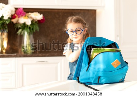 Cute child get ready for school at home sunny morning kitchen.Schoolgirl holds backpack for school day.Education,learning.Back to school.End of epidemic Coronavirus.Hello autumn Royalty-Free Stock Photo #2001048458
