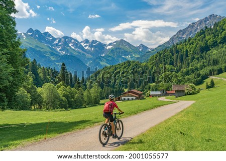 nice senior woman on mountain bike climbing up Mount Fellhorn in the Allgaeu High Alps with Trettach and Maedelegabel in background, Allgau, Bavaria, Germany Royalty-Free Stock Photo #2001055577