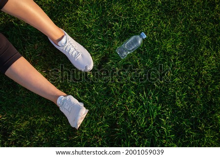 Woman is lying on the green lawn in the park. Happy woman relaxing on the grass during sunny summer day. Women's feet in white sneakers.
Top view. large format banner