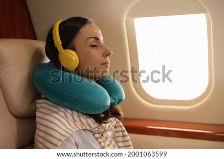 Young woman with travel pillow resting while listening to music in airplane during flight Royalty-Free Stock Photo #2001063599