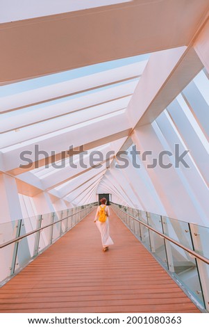 Happy woman tourist walking and admiring the unique interior of the pedestrian bridge over the water channel in Dubai, UAE Royalty-Free Stock Photo #2001080363
