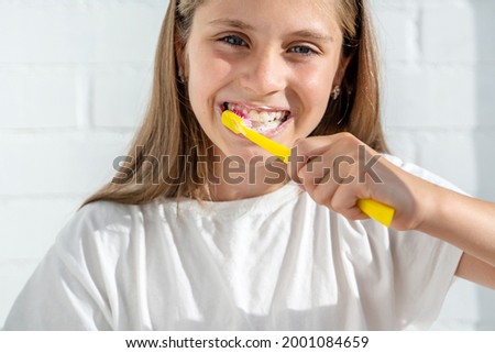 Beautiful little girl child brushing her teeth against the background of a white brick wall in a sunny bathroom. The concept of hygiene and oral care