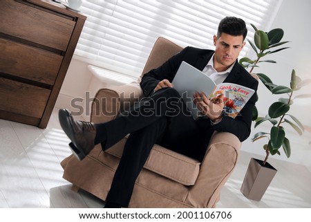 Man reading culinary magazine in armchair at home