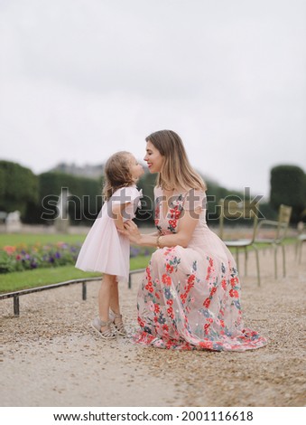 Little cute blonde girl in a pink dress is having fun with her mother in the park.