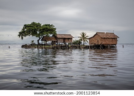 Traditional thatched houses on a small artificial island on a gloomy day in Lau Lagoon, off the island of Malaita in the Solomon Islands. Royalty-Free Stock Photo #2001123854